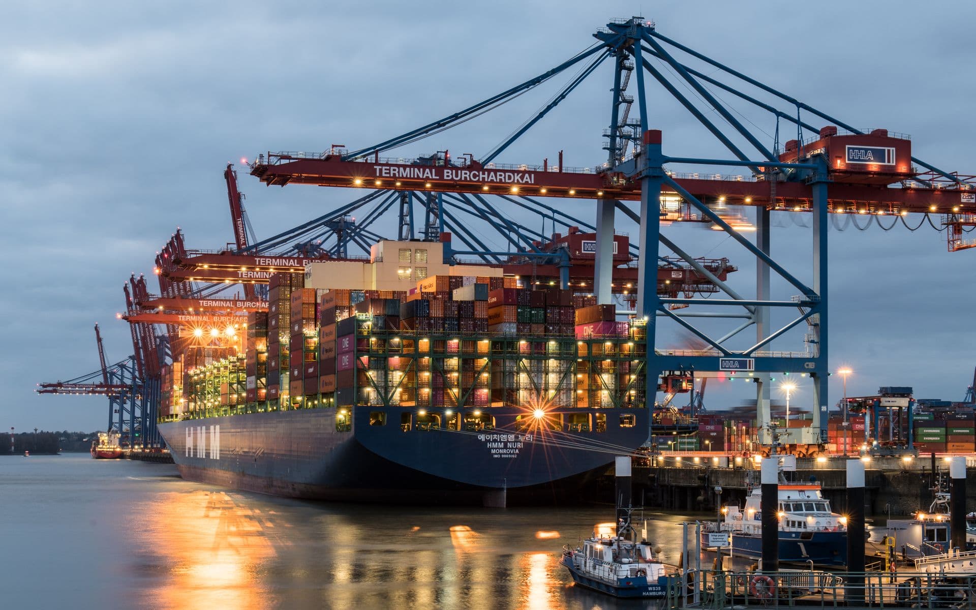 Container ship at a marine terminal beneath gantry cranes at dusk