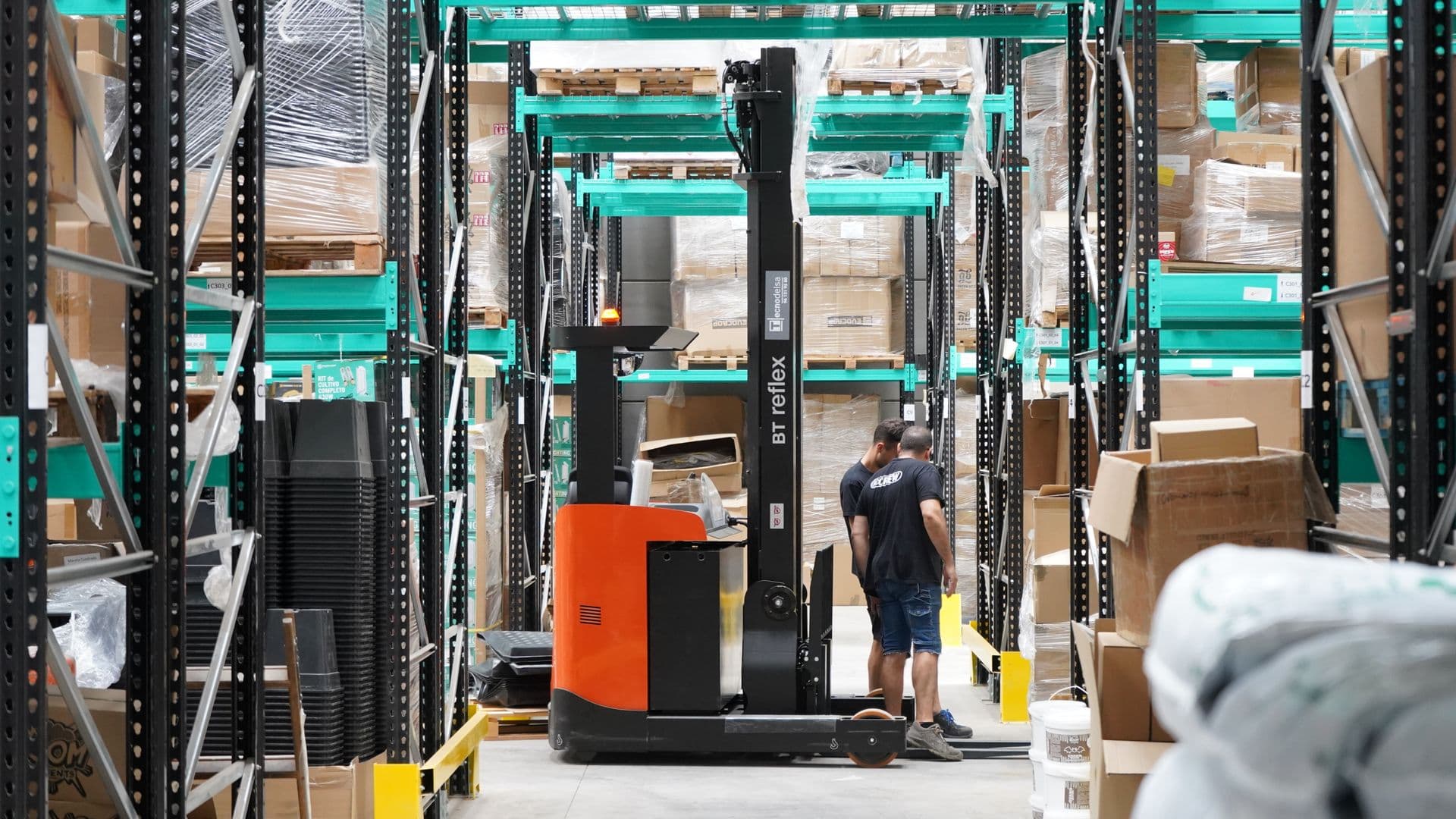 Warehouse workers and a forklift moving pallets among storage racks
