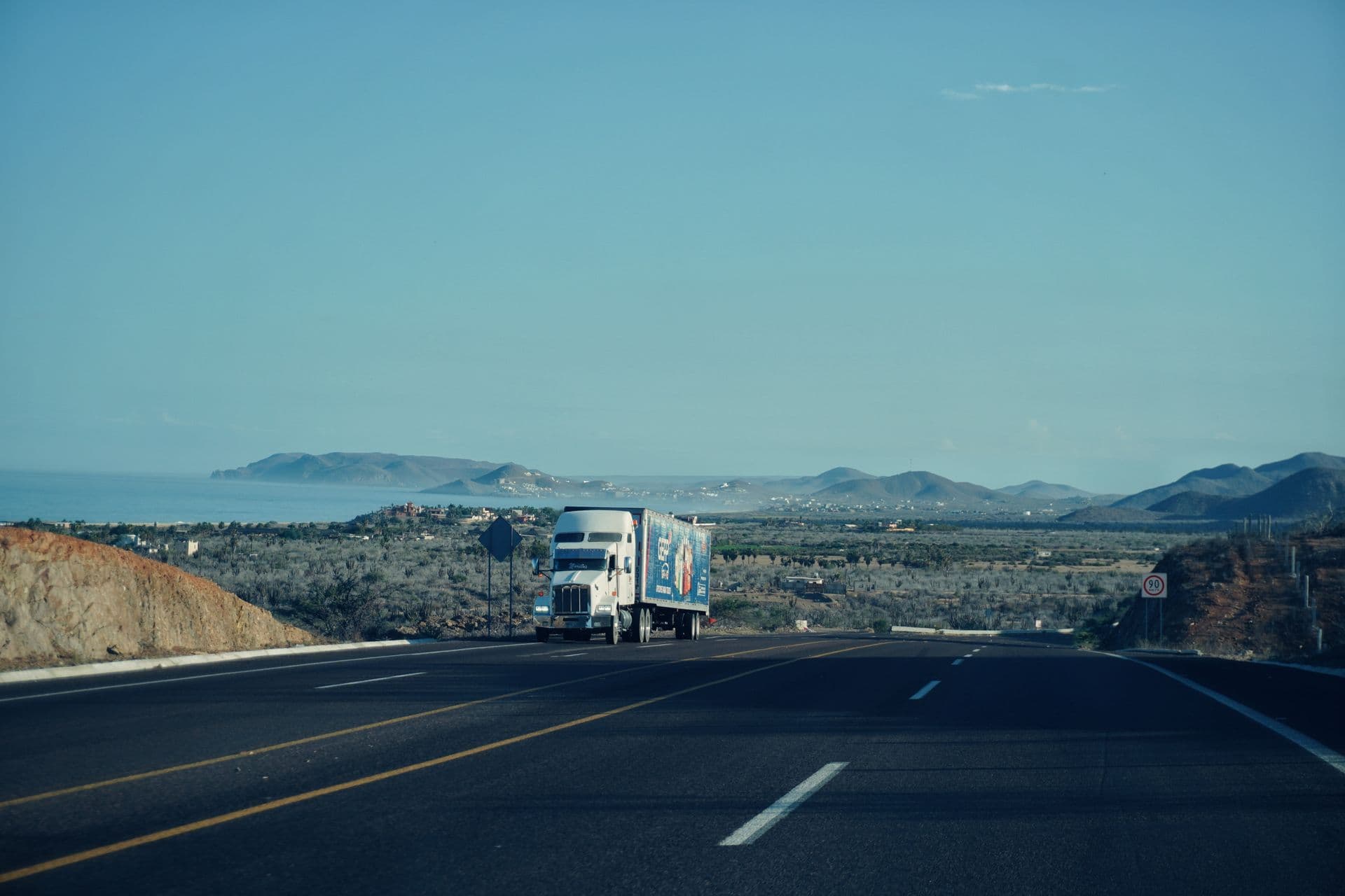 Semi truck on a coastal highway with mountains in the background
